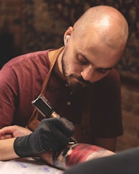 a bald man getting a tattoo on his arm